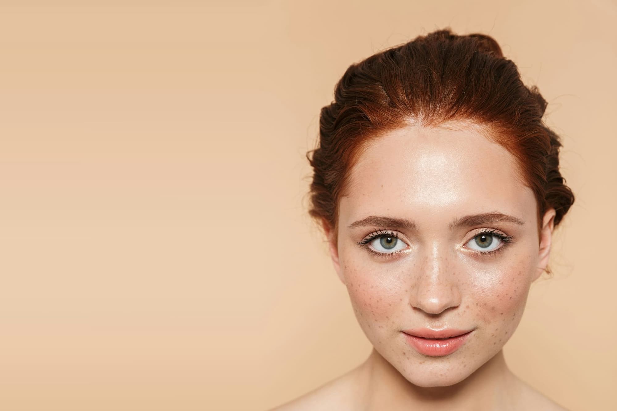 Woman with freckles and luminous, natural-looking skin against a warm peach backdrop