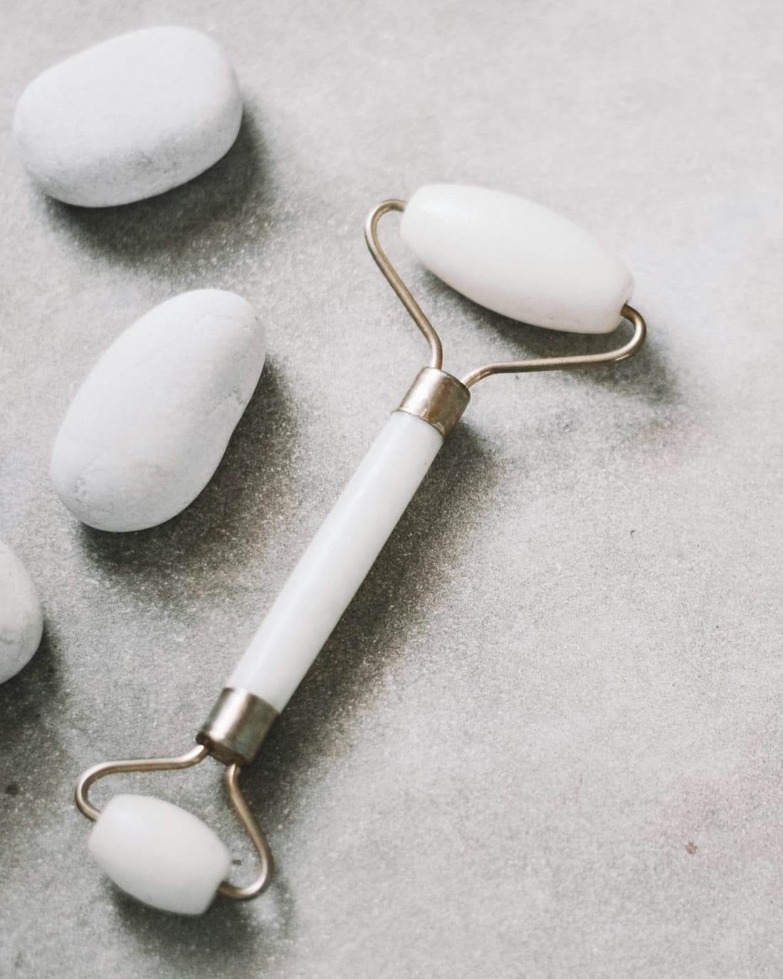 White stone facial roller beside smooth white stones on a gray stone surface